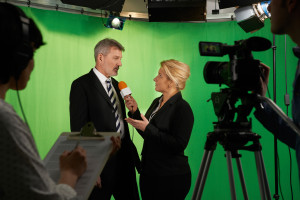 Female Presenter Interviewing In Television Studio With Crew In Foreground